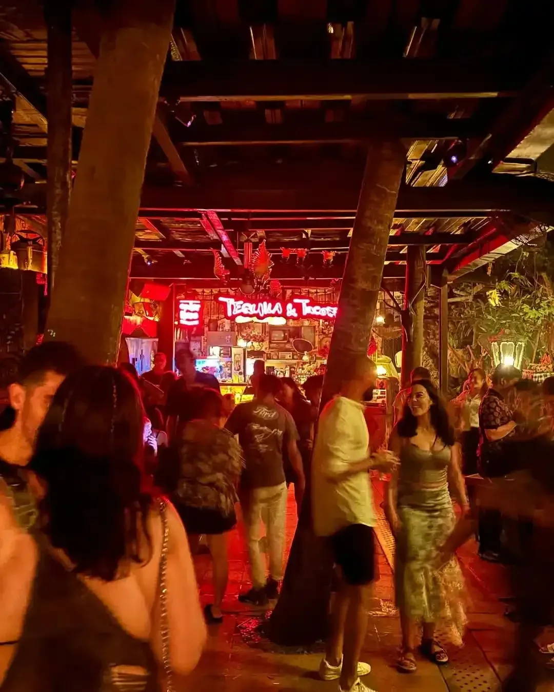 Crowded night floor at La Favela in Seminyak under red neon, with the bar visible through the wooden columns
